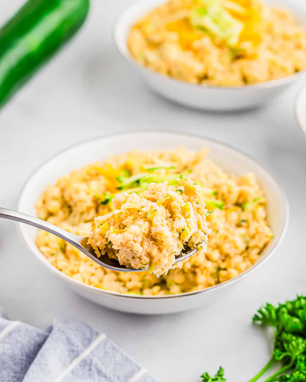 A bowl of cheesy quinoa and zucchini with a spoon.