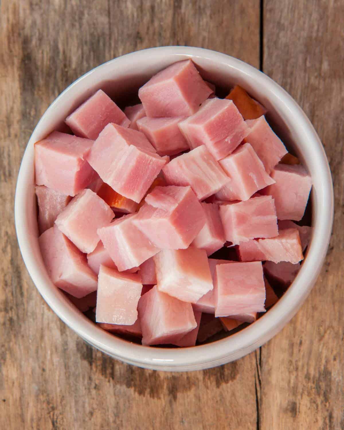Ham cubes in a bowl on a wooden table.