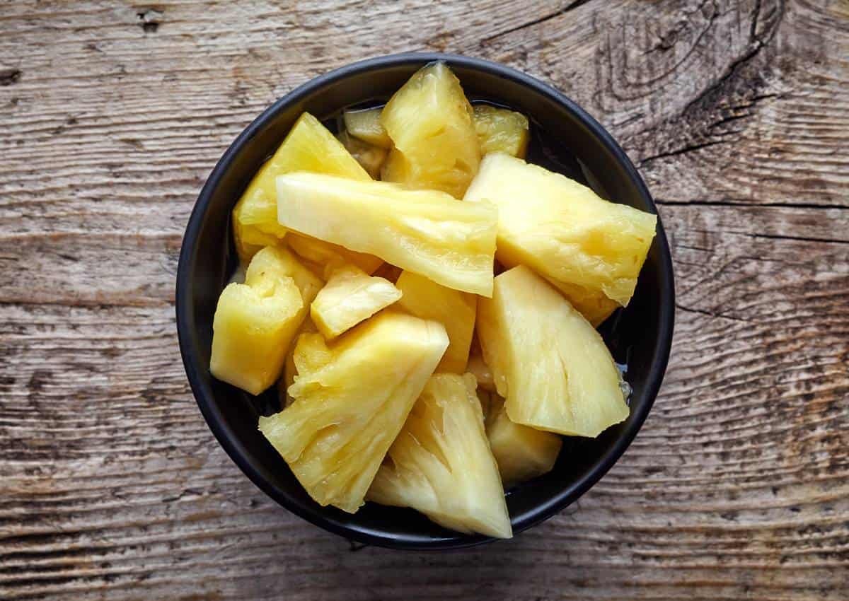 Pineapple slices in a bowl on a wooden table.