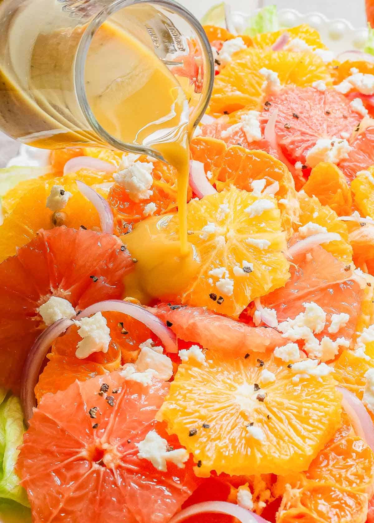 A plate of oranges and grapefruits over salad with a dressing being poured on it.