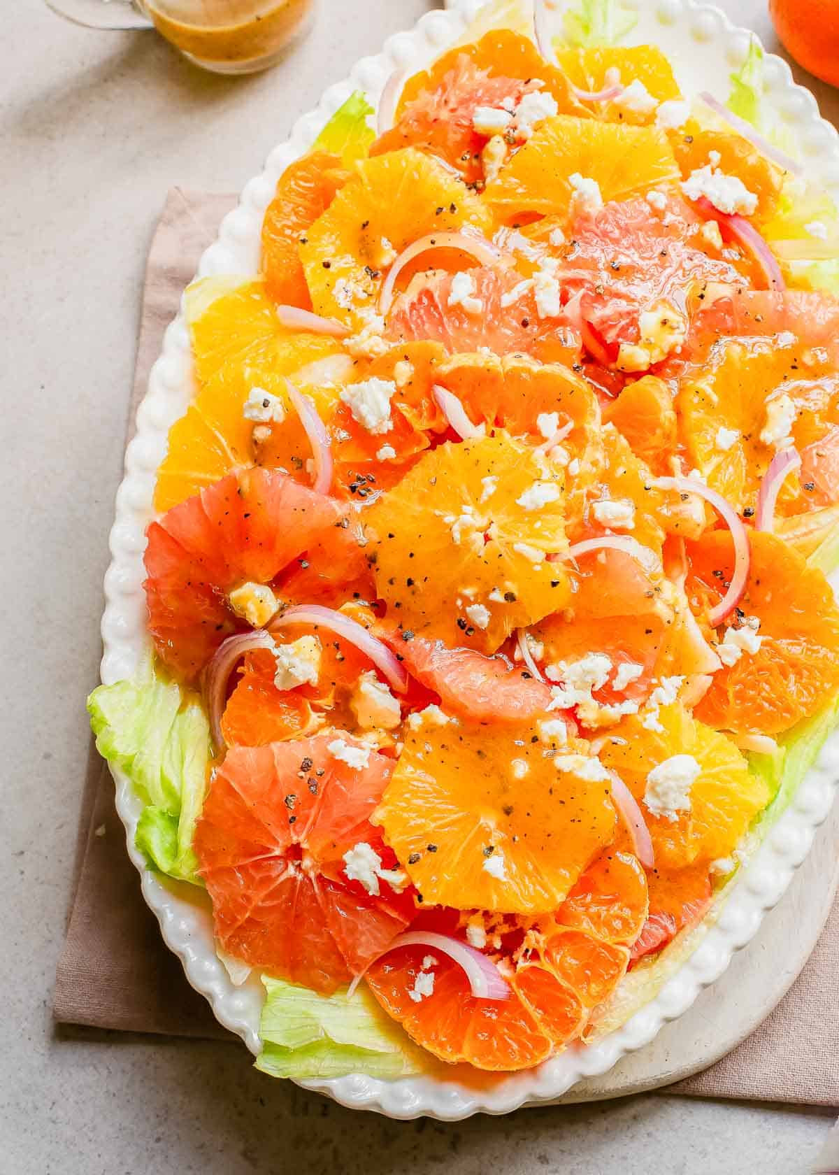 Citrus salad with feta and onions on a white platter.