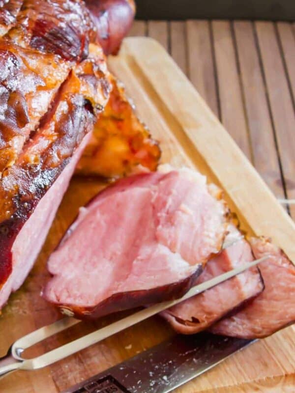A ham on a cutting board with a knife.
