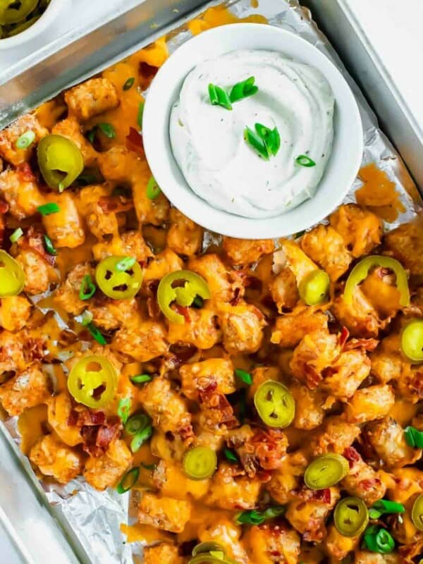 Cheesy bacon nachos in a foil pan with dipping sauce.