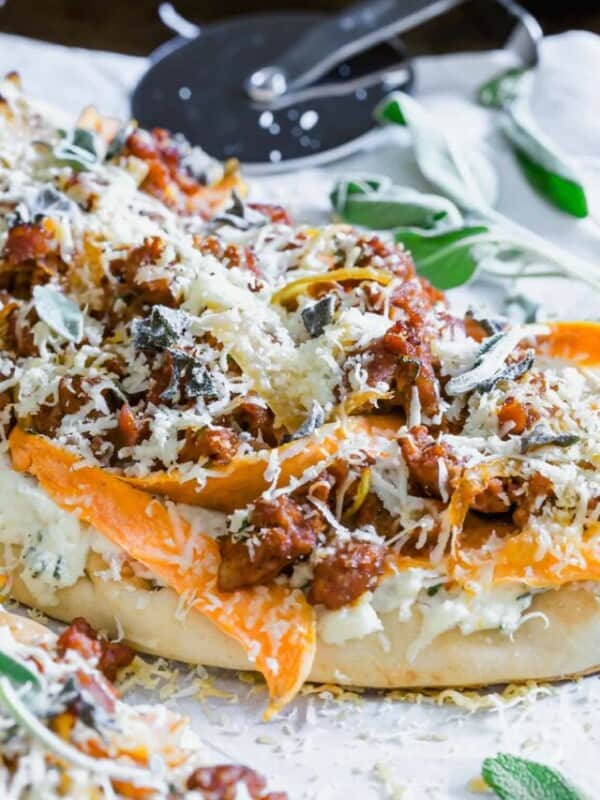 A pizza with meat, cheese and sage.