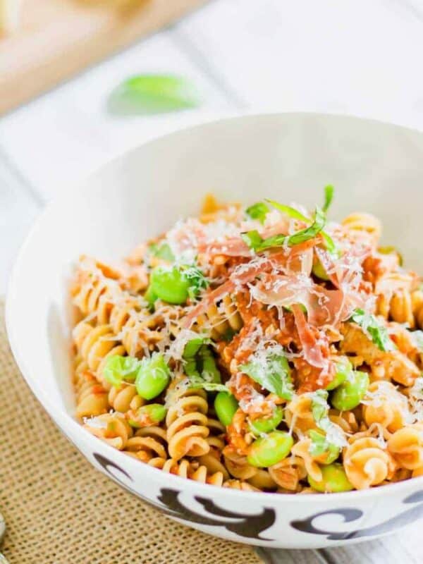 A bowl of pasta with peas and ham.