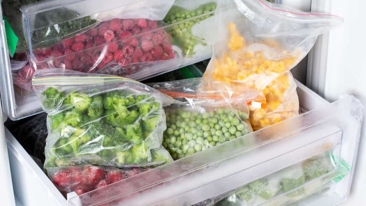 A refrigerator full of vegetables and fruit in plastic bags.