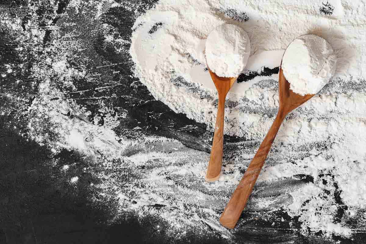 Two wooden spoons next to a bowl of flour.