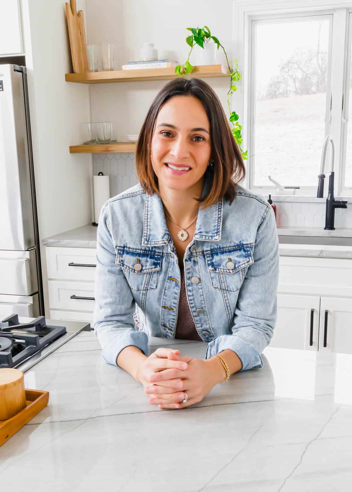 Gina Matsoukas in a denim jacket sitting at a kitchen counter.