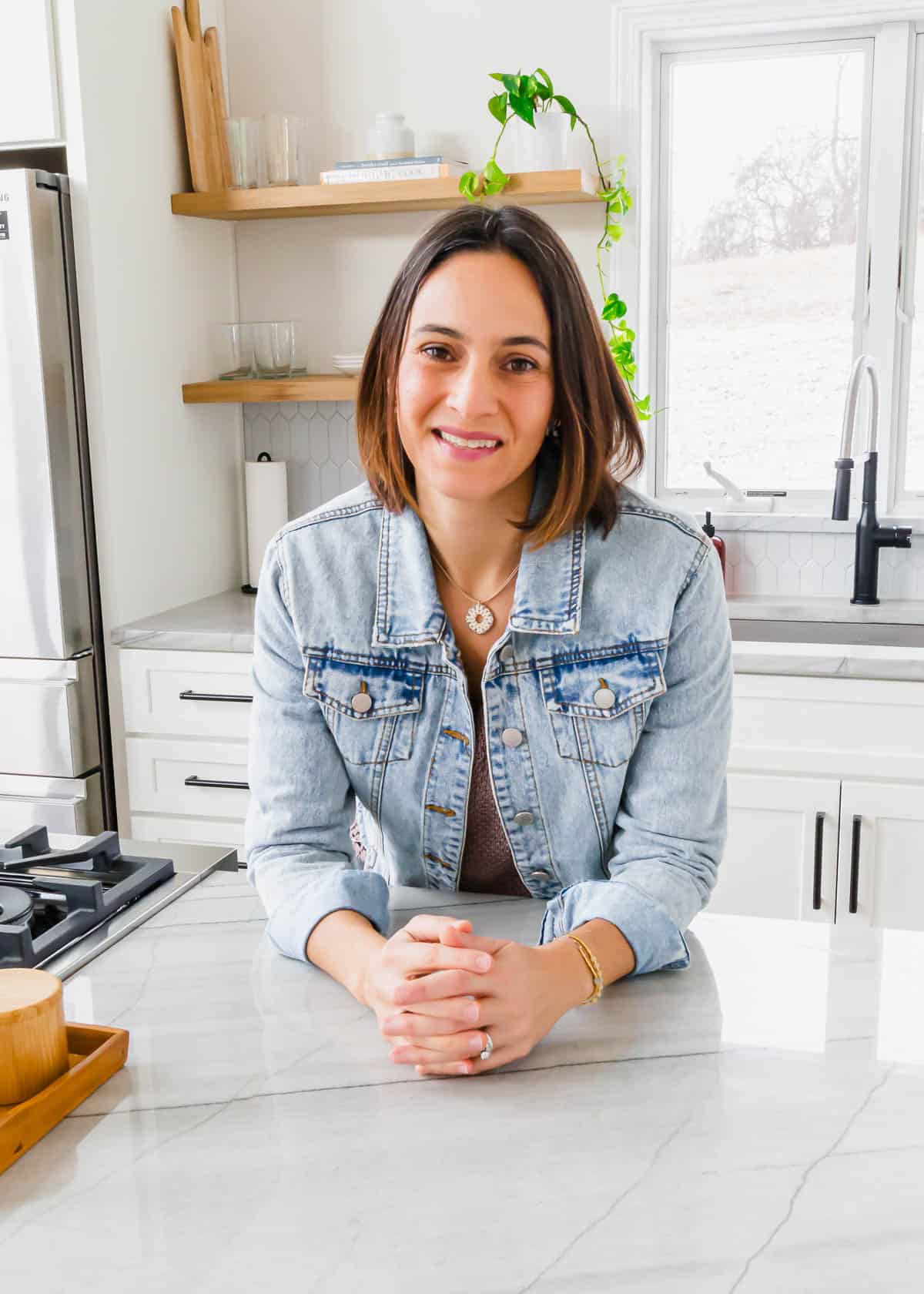 A woman in a denim jacket sitting at a kitchen counter, preparing wholesome fresh recipes.