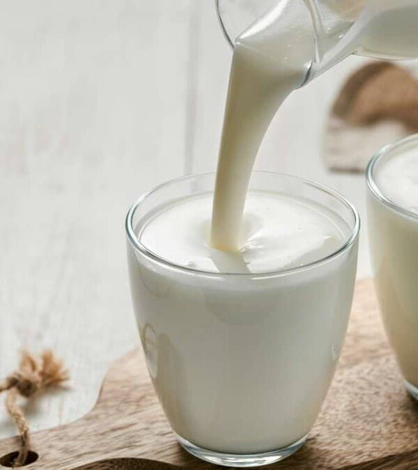 Two glasses of kefir being poured on a wooden table.