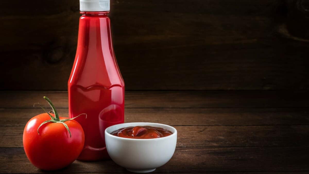 A bottle of tomato sauce and a cup of tomatoes on a wooden table.