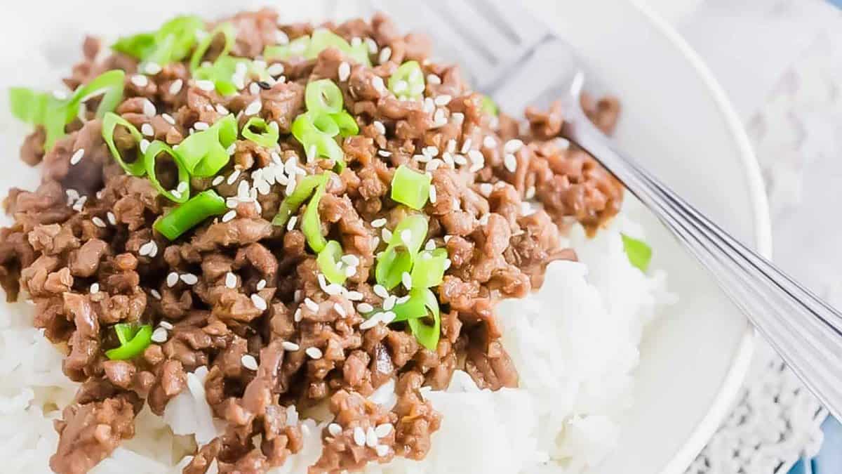 A plate of rice with beef and green onions on it.