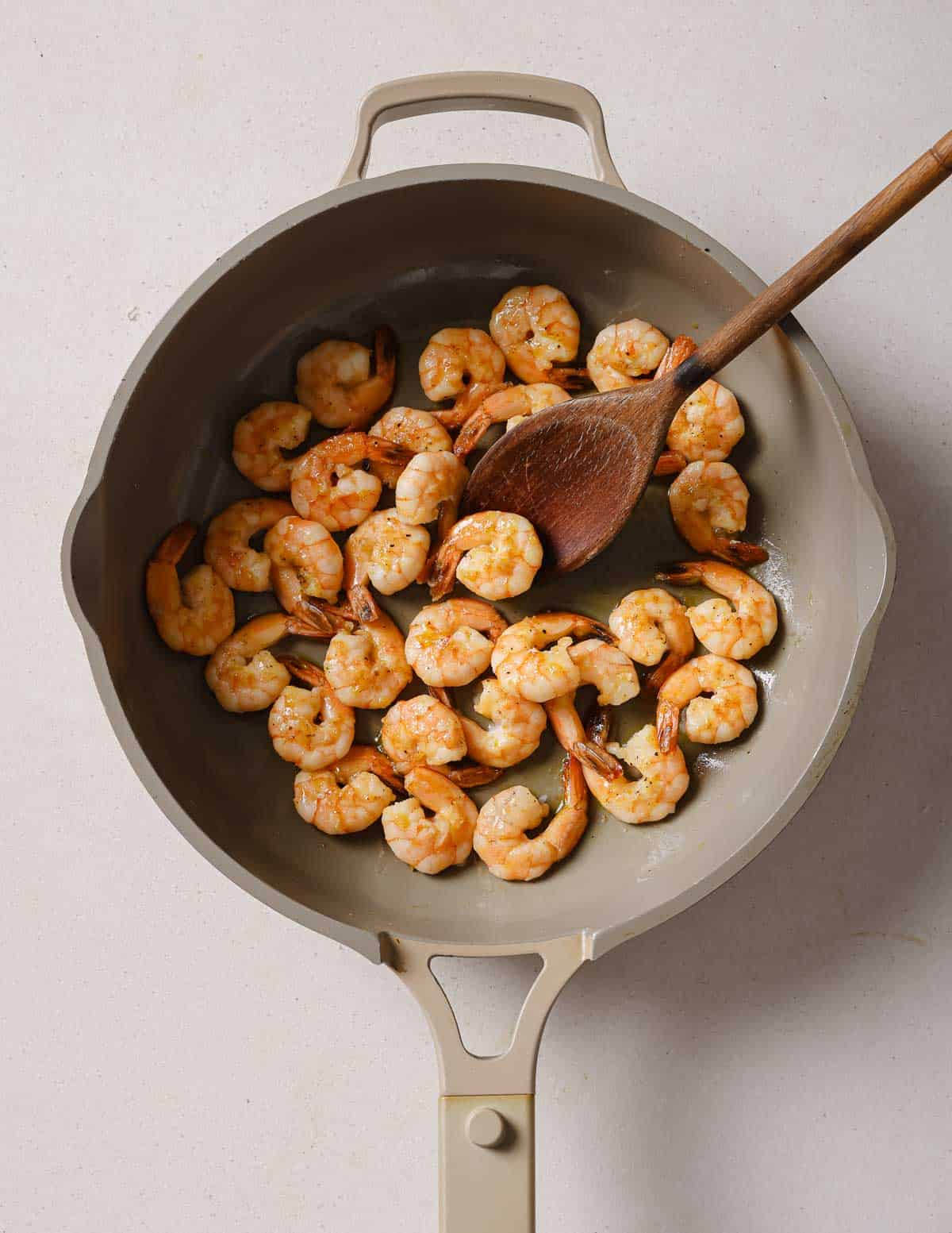 Shrimp in a frying pan with a wooden spoon.