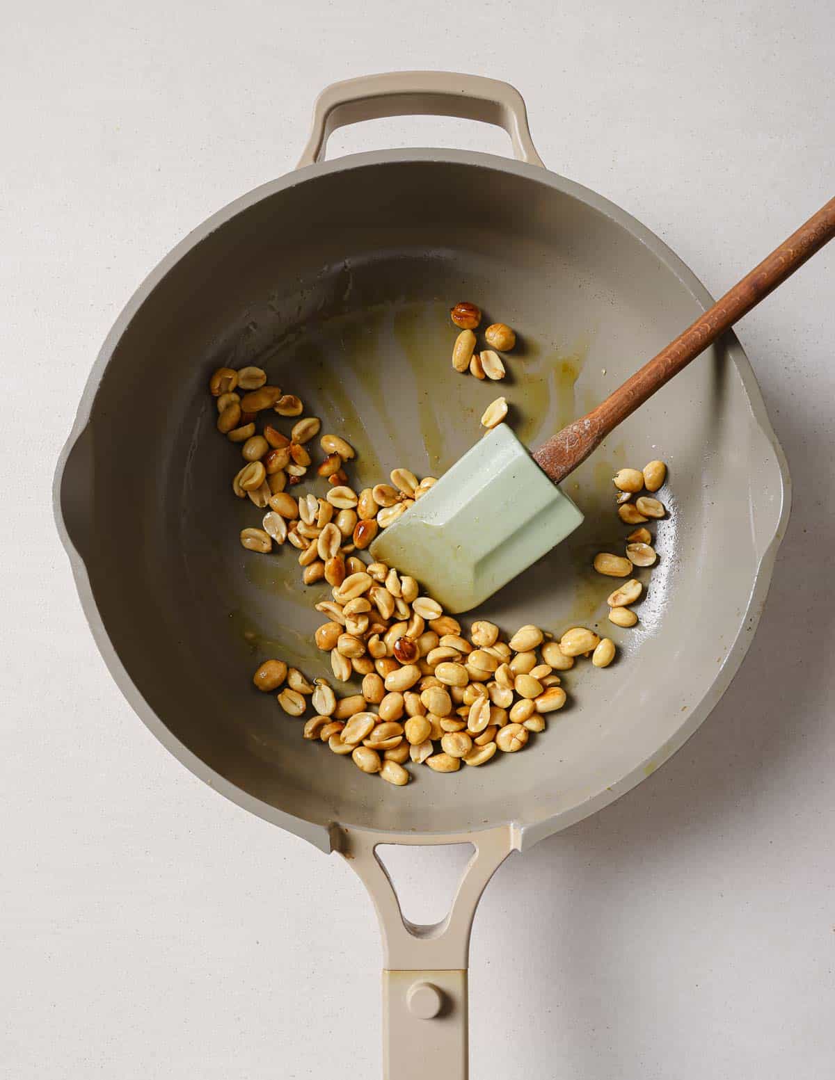 A frying pan filled with peanuts and a wooden spoon.