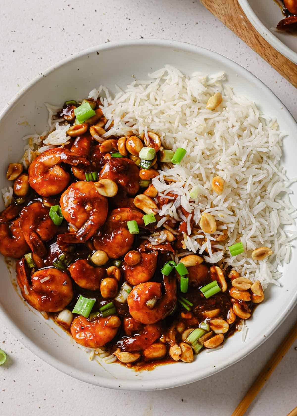 A white bowl with rice and kung pao shrimp in it.