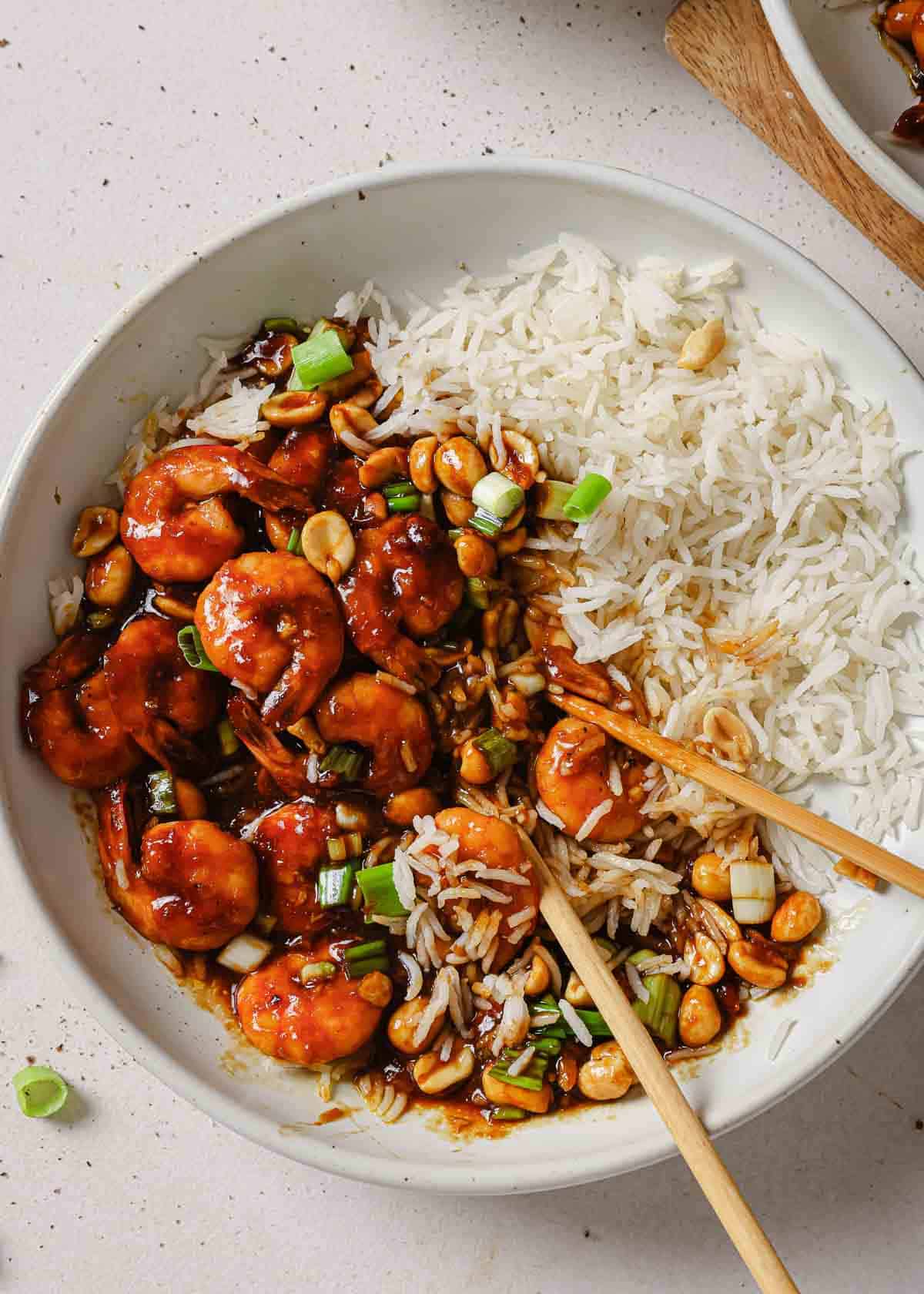 A bowl of white rice and shrimp with kung pao sauce with chopsticks.