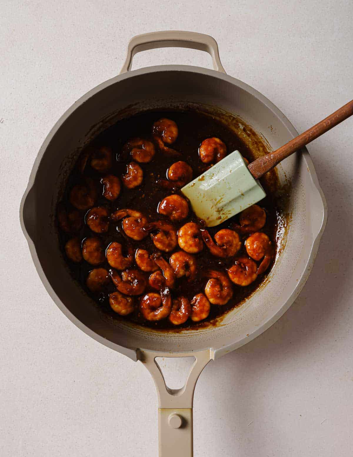 A frying pan with shrimp in it and a spatula.