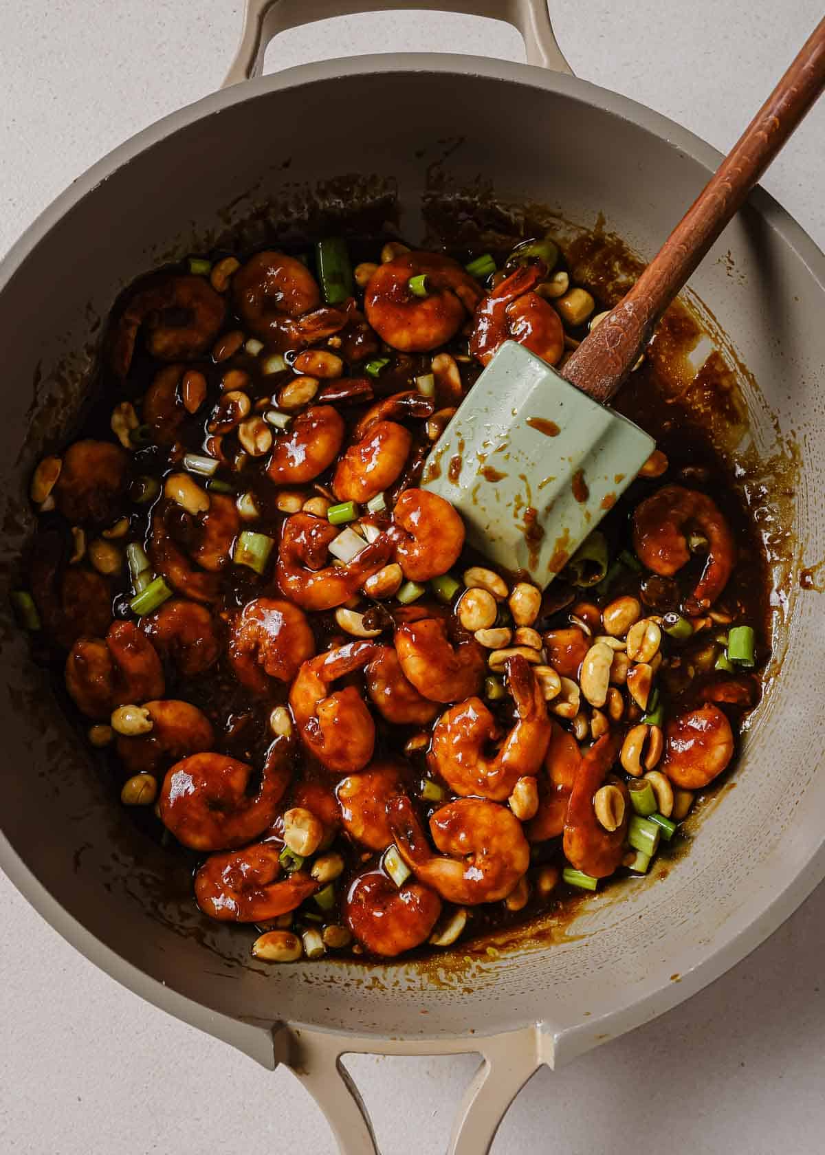 Chinese kung pao shrimp in a wok with a wooden spoon.