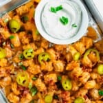 A baking sheet with tater tots, bacon, cheese, and jalapenos.