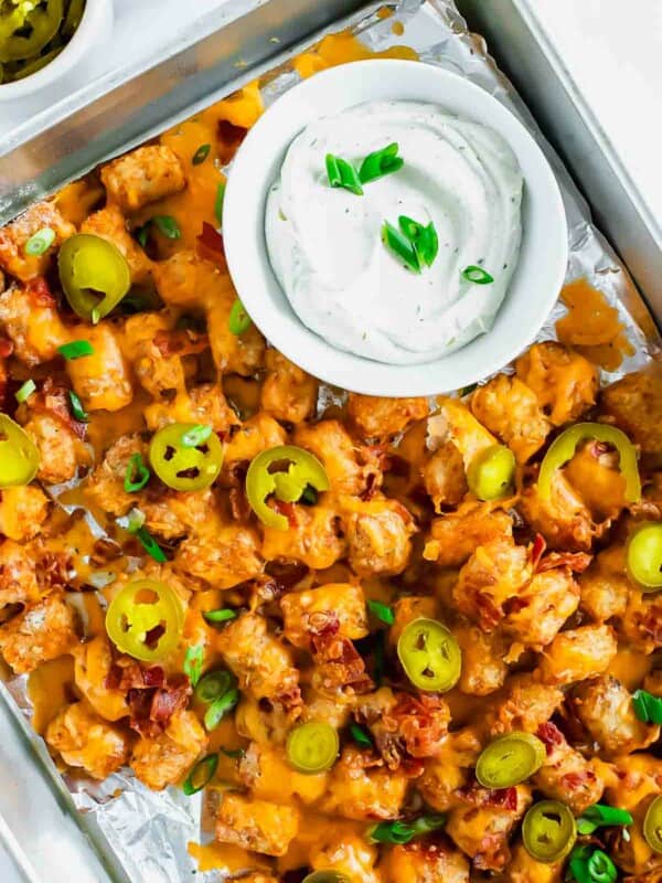 A baking sheet with tater tots, bacon, cheese, and jalapenos.