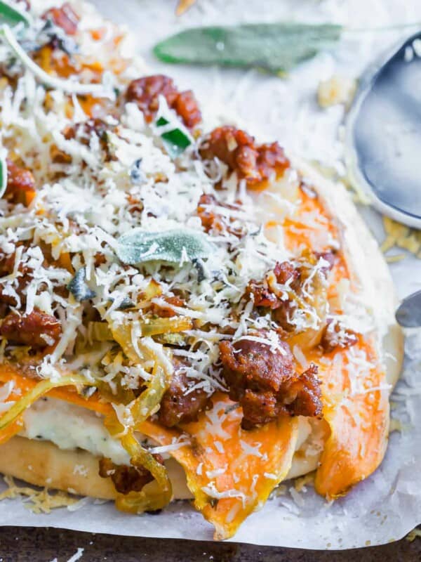 A pizza on a piece of parchment paper with sweet potato and chorizo.