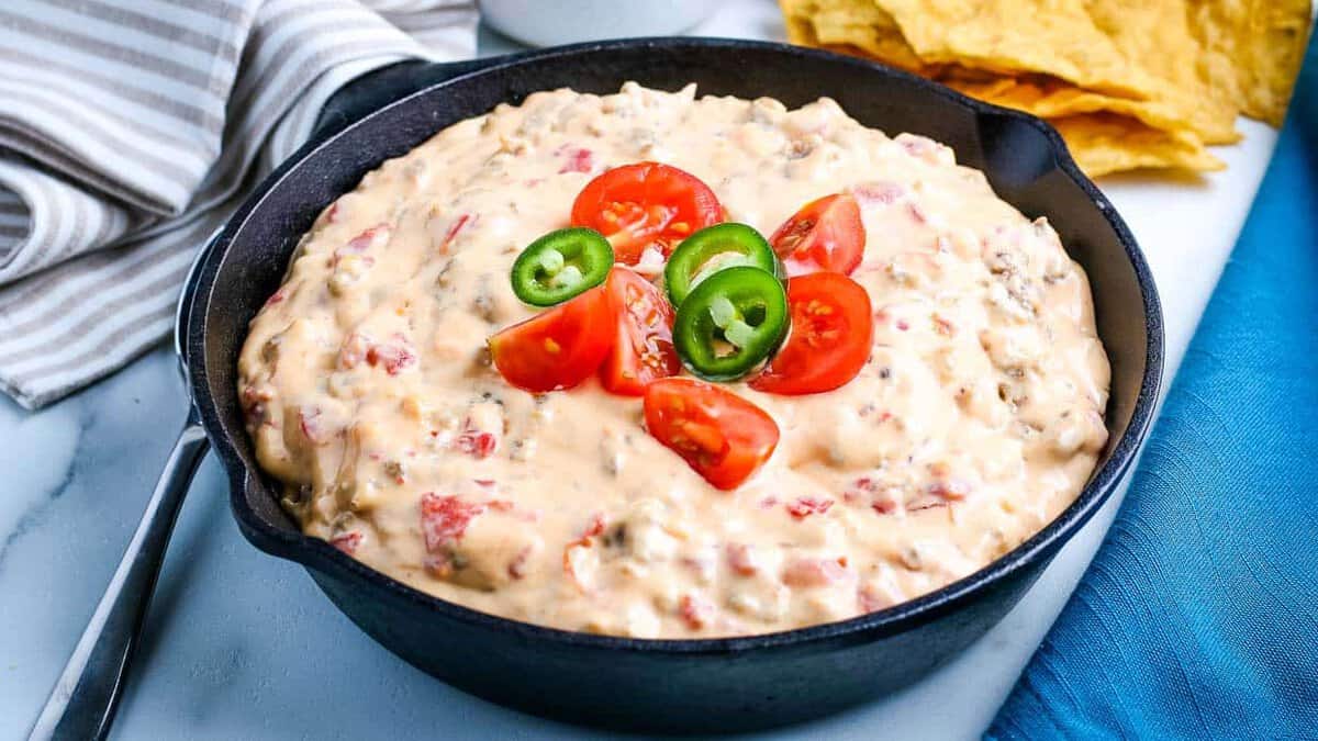 Sausage cheese dip in a cast iron skillet topped with tomatoes and jalapenos.
