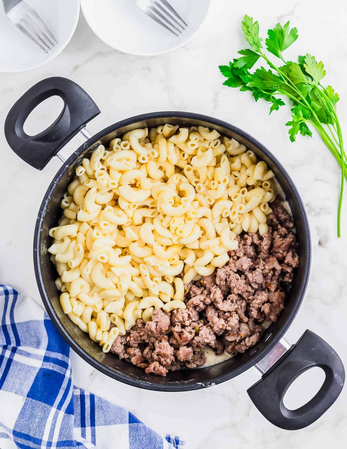 Macaroni and cheese in a skillet with sausage and parsley.