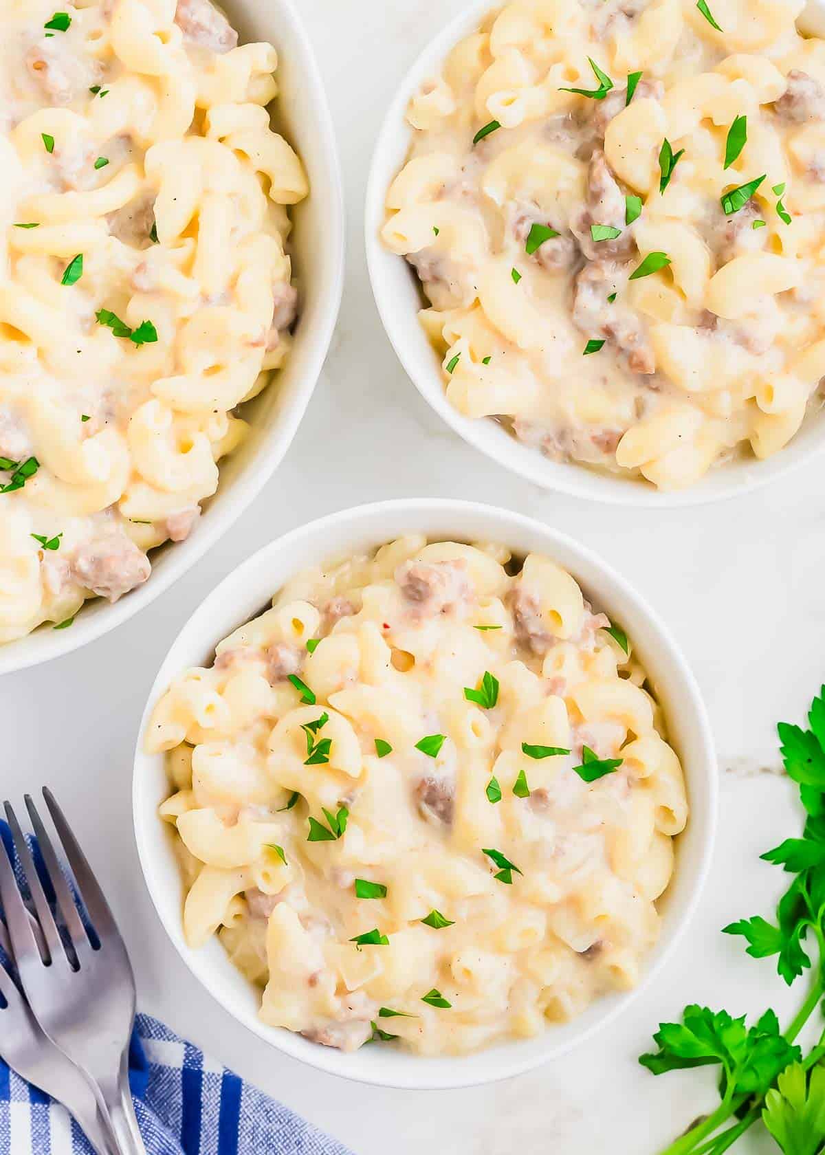Three bowls of macaroni and cheese with sausage and parsley.