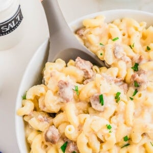 Sausage macaroni and cheese in a white bowl with a wooden and rubber spoon.