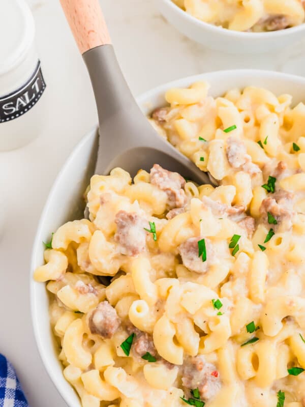 Sausage macaroni and cheese in a white bowl with a wooden and rubber spoon.