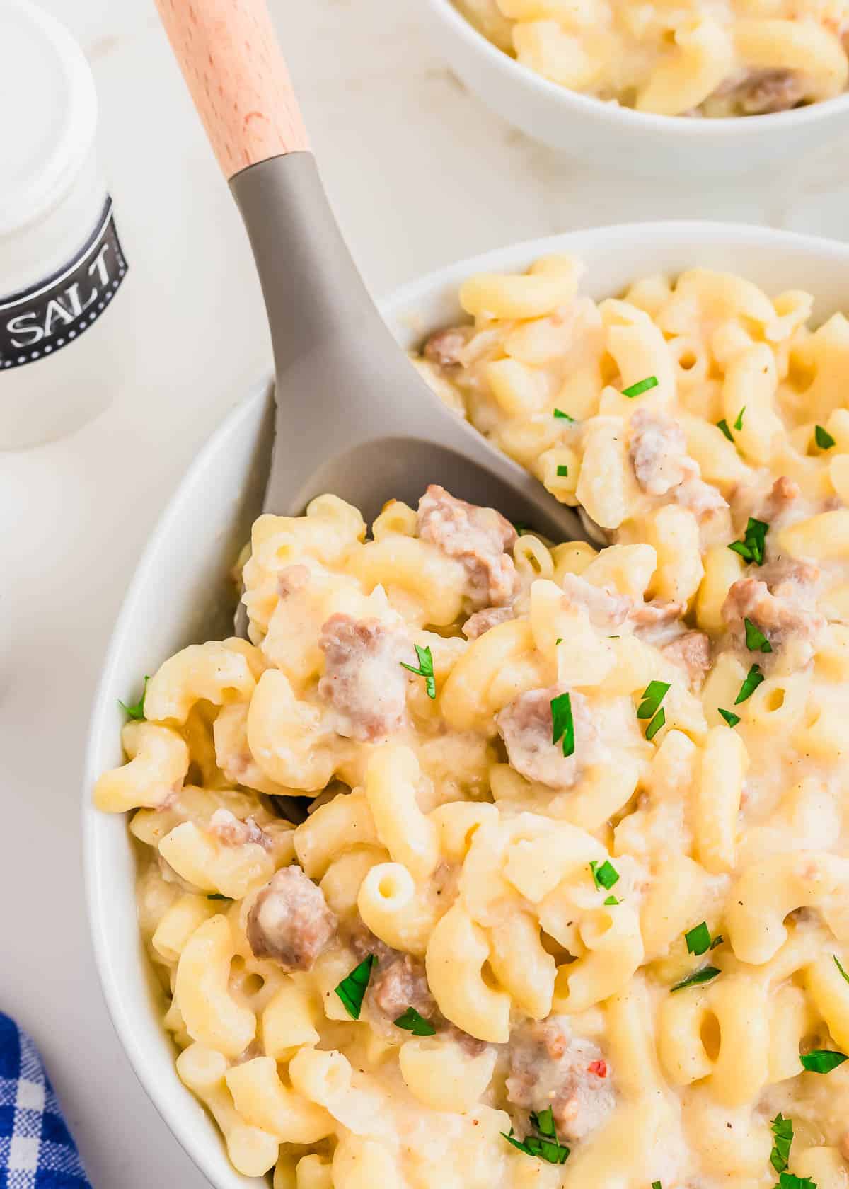 Sausage macaroni and cheese in a white bowl with a wooden and rubber spoon.