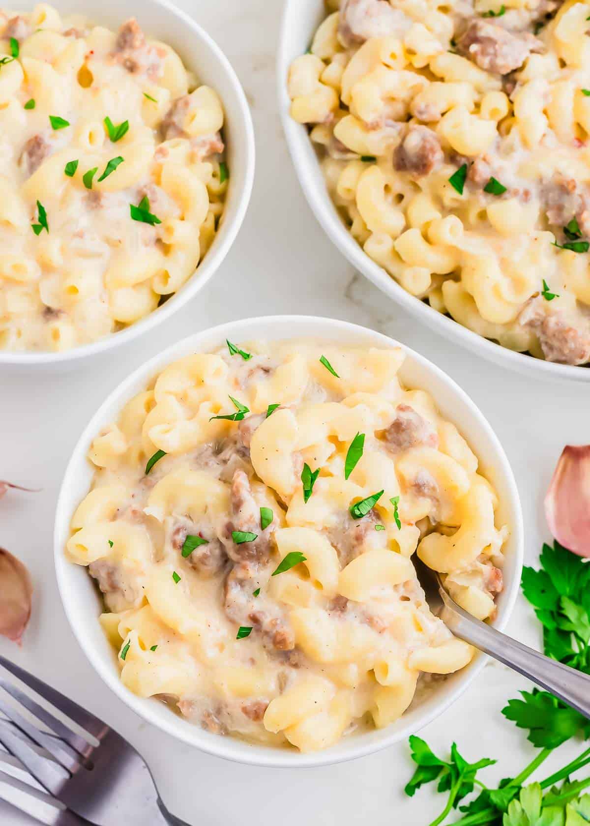 Three bowls of macaroni and cheese with sausage and parsley.