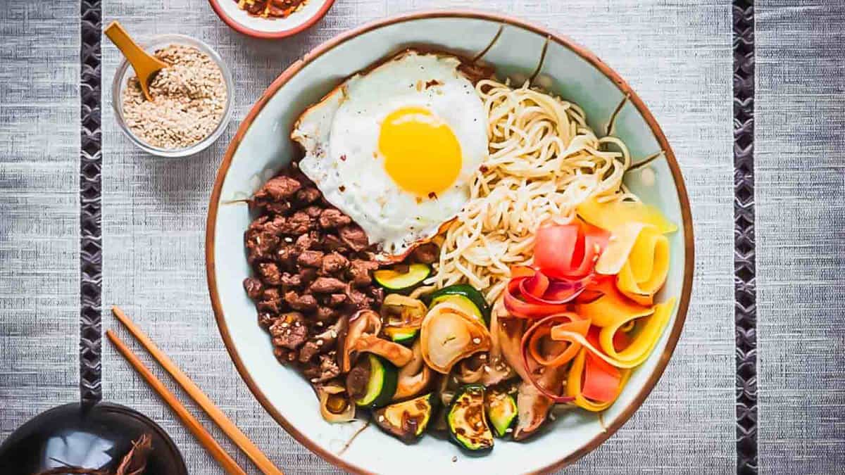 A bowl of noodles and vegetables with an egg on top.