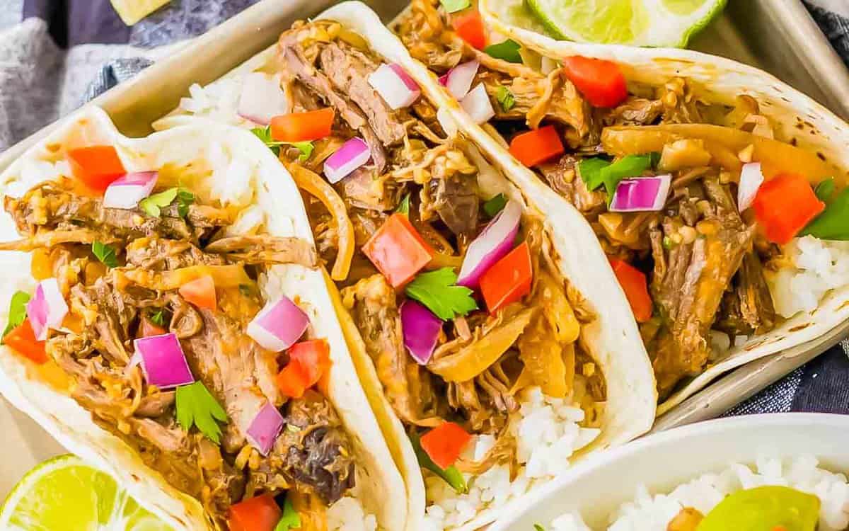 Barbacoa tacos on a tray topped with peppers and onions.