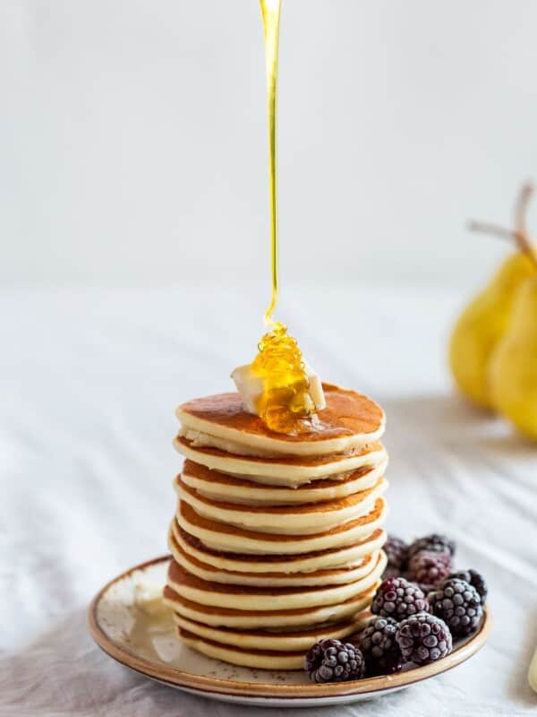A stack of pancakes with honey being poured over them.