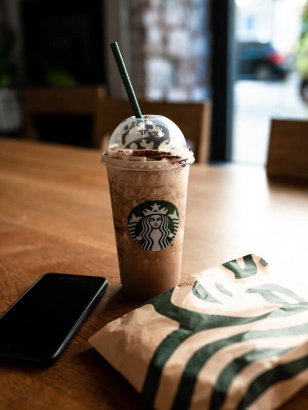 A starbucks drink on a table next to a cell phone.
