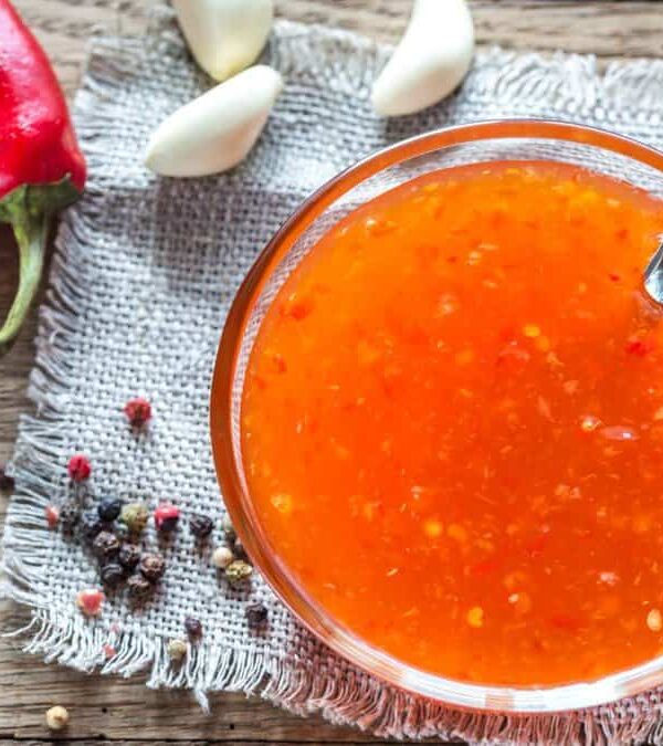 A bowl of hot sauce with peppers and garlic on a wooden table.