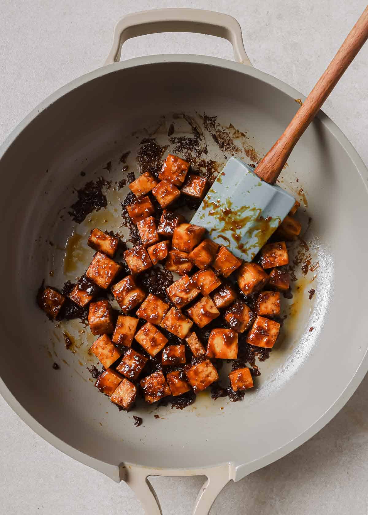 Tofu in a wok with a wooden spoon.