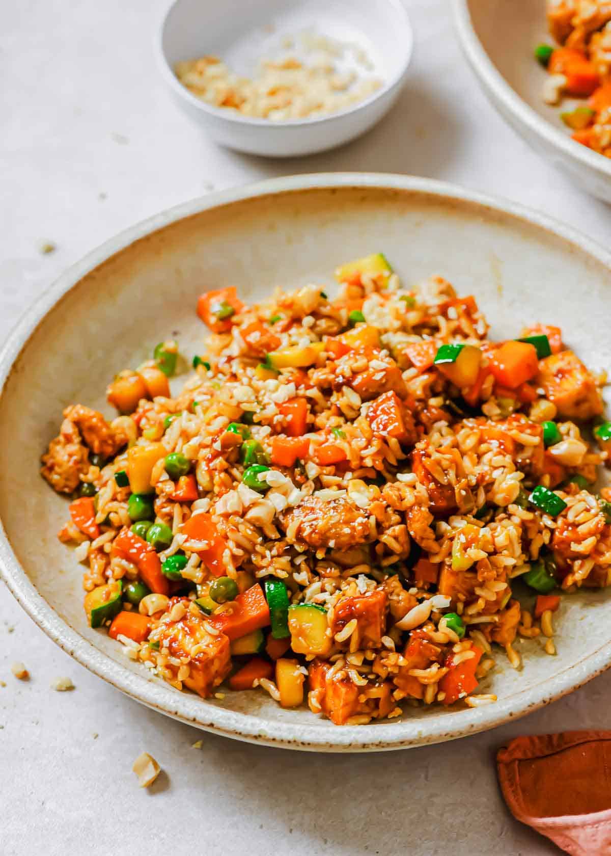 Two bowls of fried rice with vegetables and a small bowl of crushed nuts in the background.