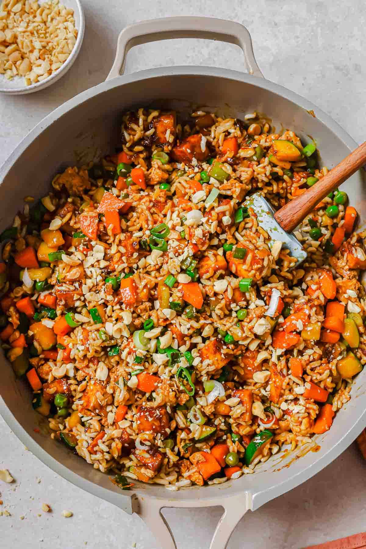 A pan full of fried rice with tofu and vegetables and a wooden spoon.