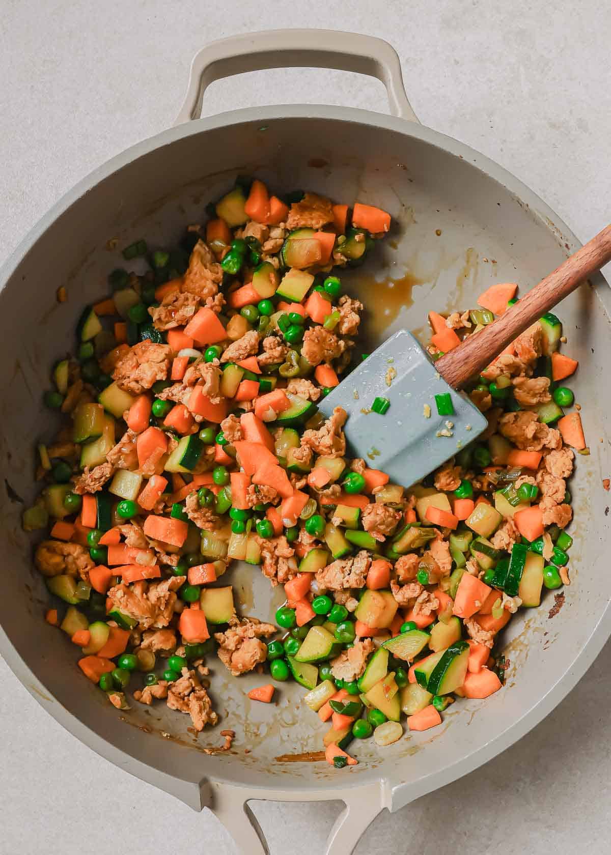Stir-fried vegetables in a wok with a wooden spatula.