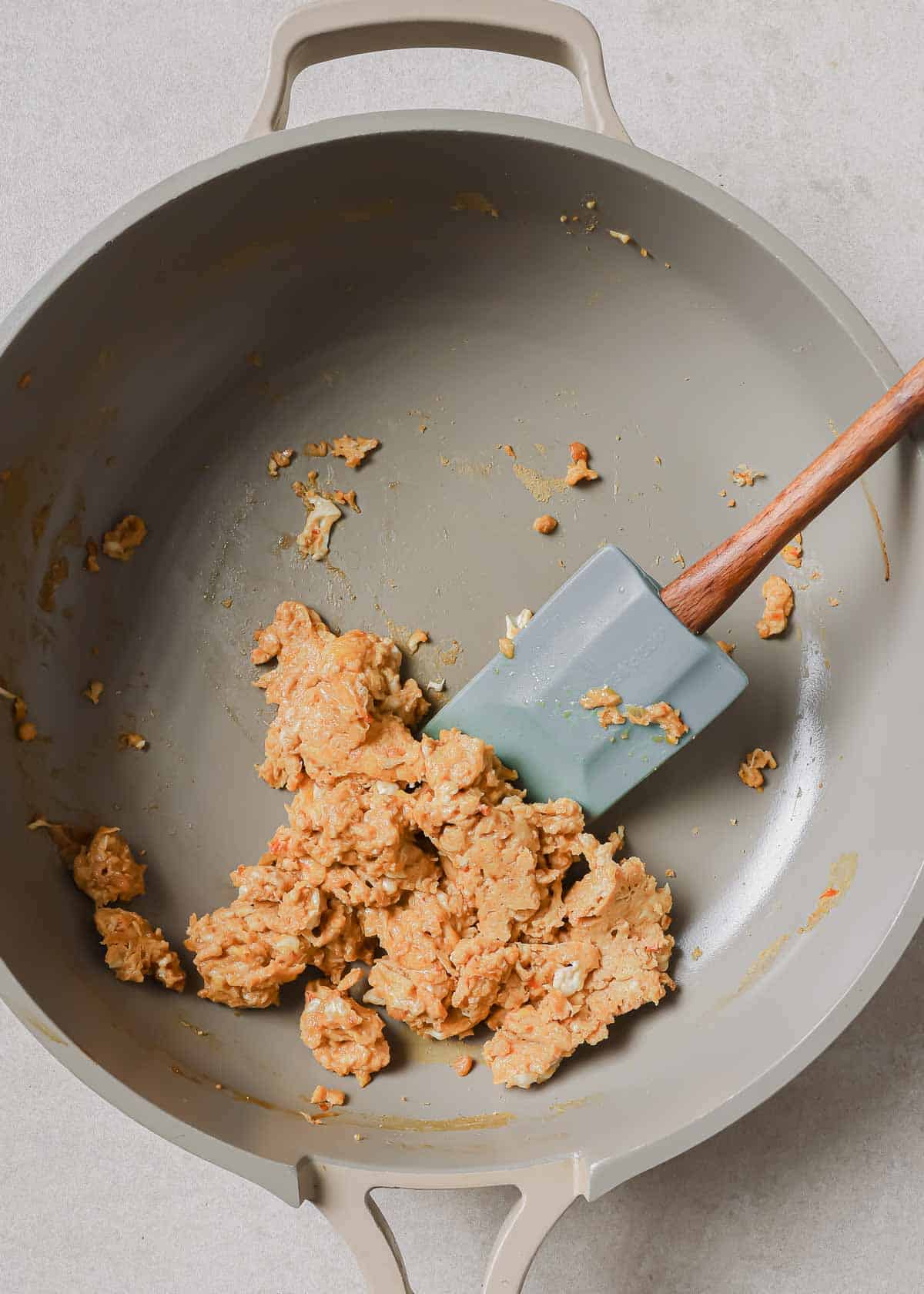 A wok with scrambled eggs and a wooden spatula in it.