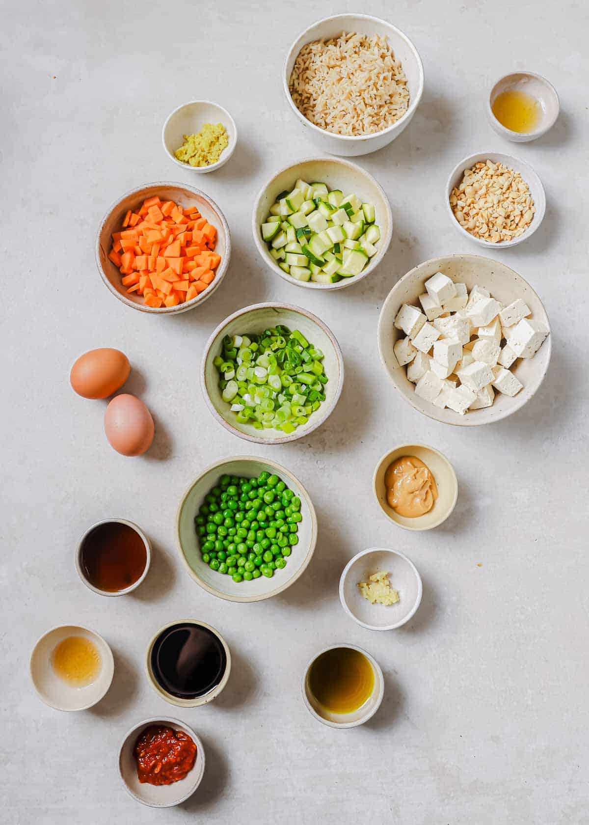 Ingredients in small bowls to make tofu fried rice on a white surface.