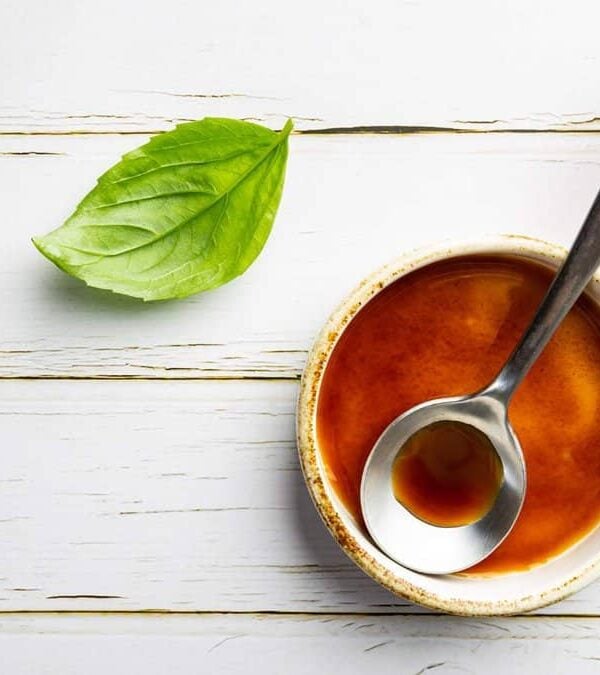 A bowl of sauce with a spoon next to a bottle of beer.