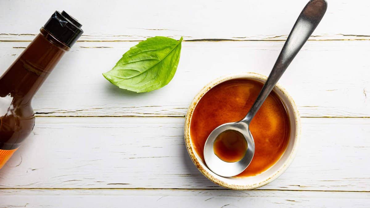 A bowl of sauce with a spoon next to a bottle of beer.