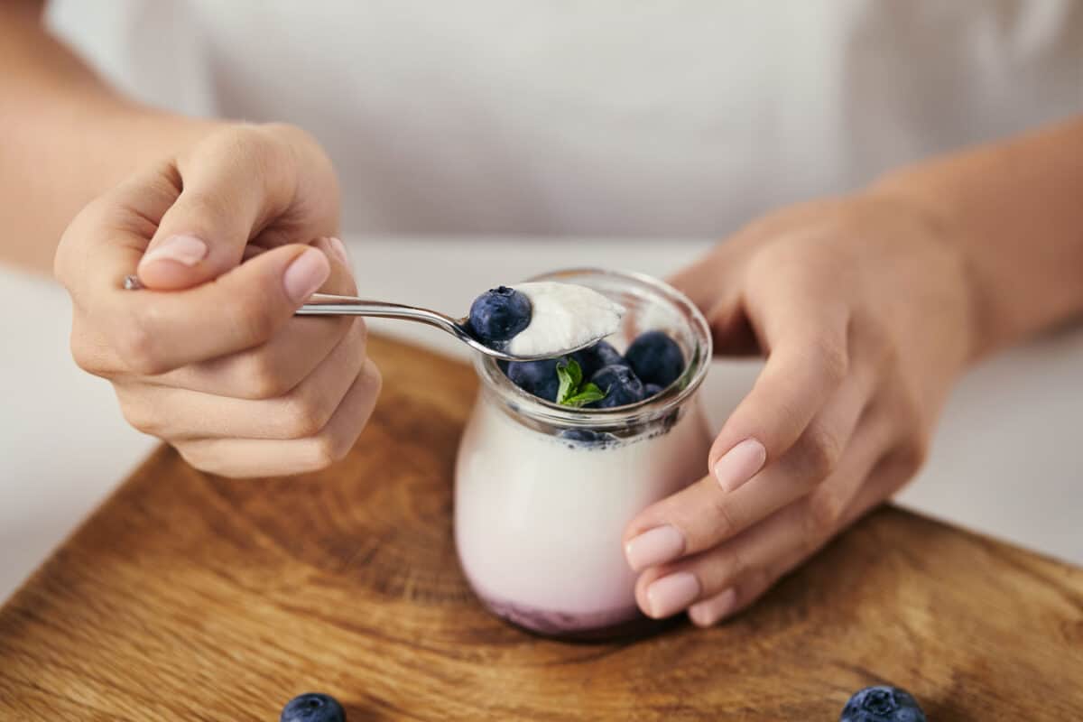 A woman's hand is holding a jar of yogurt with blueberries.