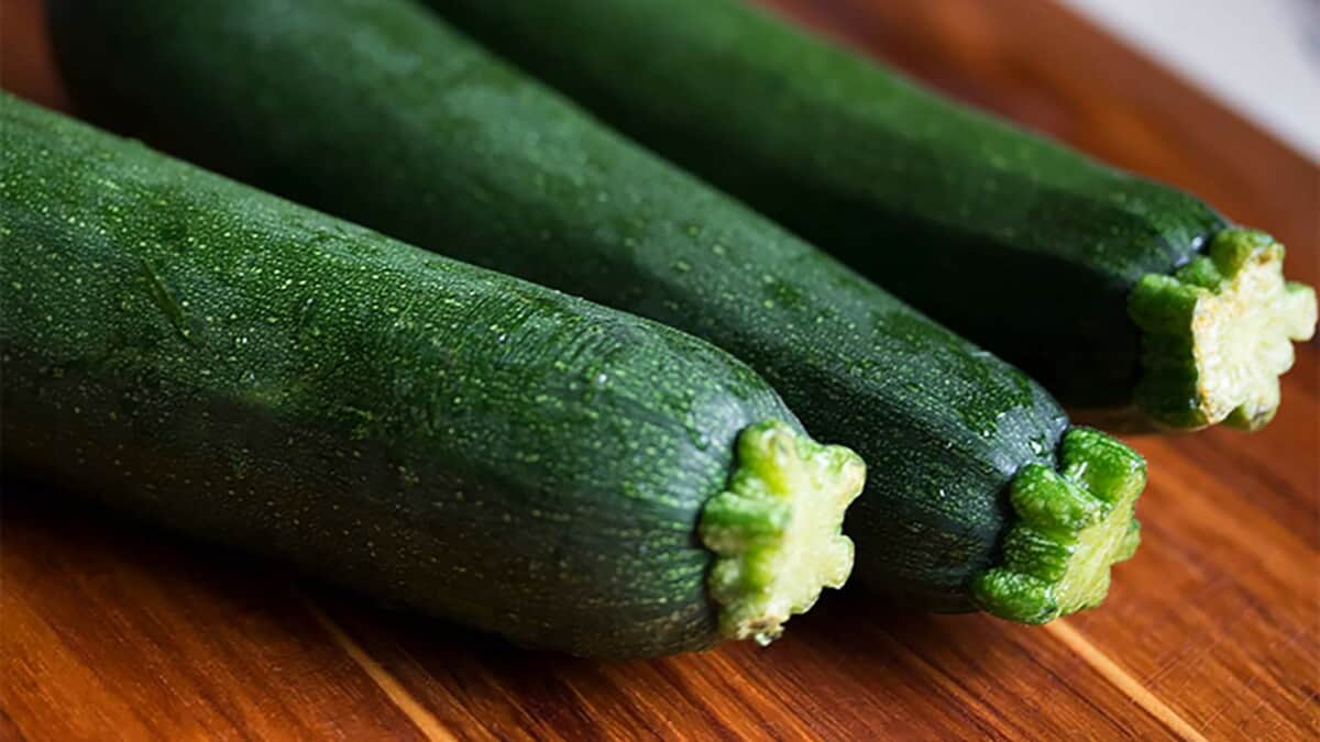 Three green zucchini sitting on a cutting board.