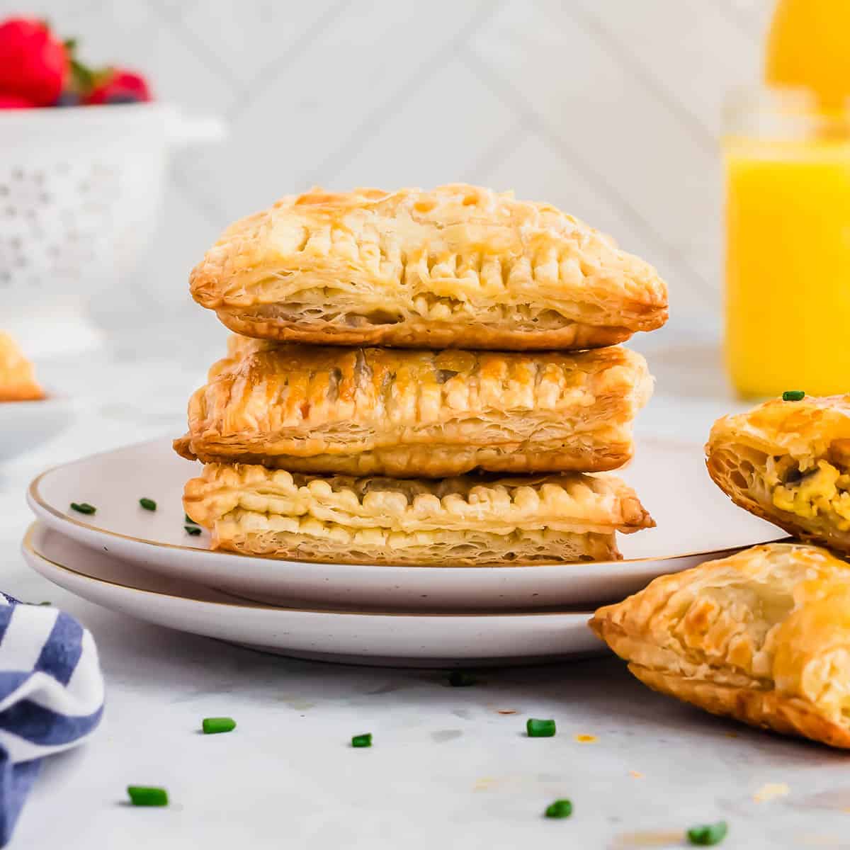 A stack of breakfast hot pocket pastries on a plate next to orange juice.