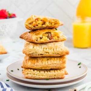 Homemade breakfast hot pockets stacked on two white plates with egg, cheese and sausage filling.