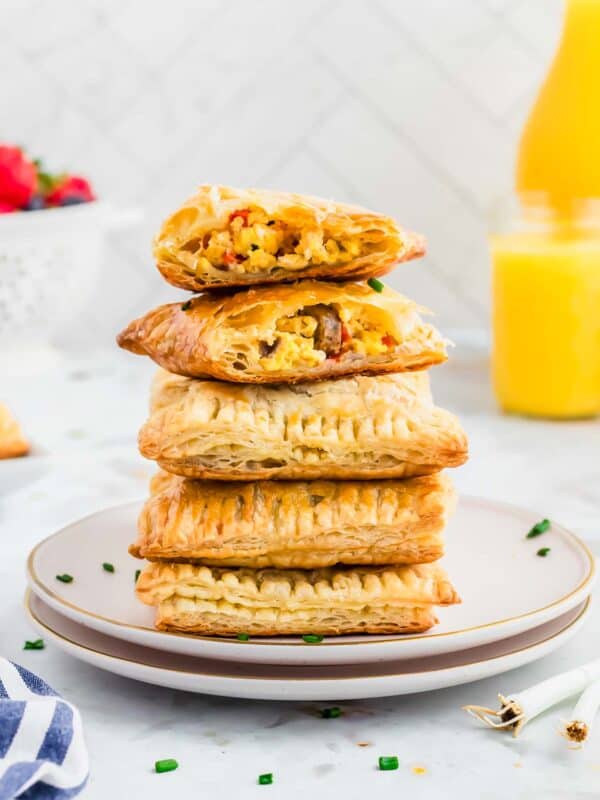 Homemade breakfast hot pockets stacked on two white plates with egg, cheese and sausage filling.